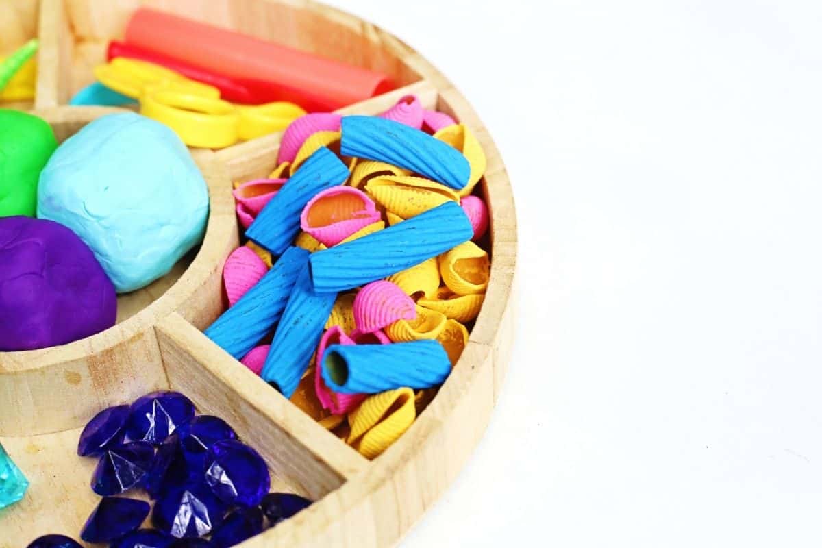 Wooden sorting tray prepared for a mermaid playdough activity with colorful playdough, shells, blue gems, toy scissors, and textured sea themed loose parts. The organized sensory materials invite children to build underwater mermaid worlds while exploring colors, textures, and creative play.