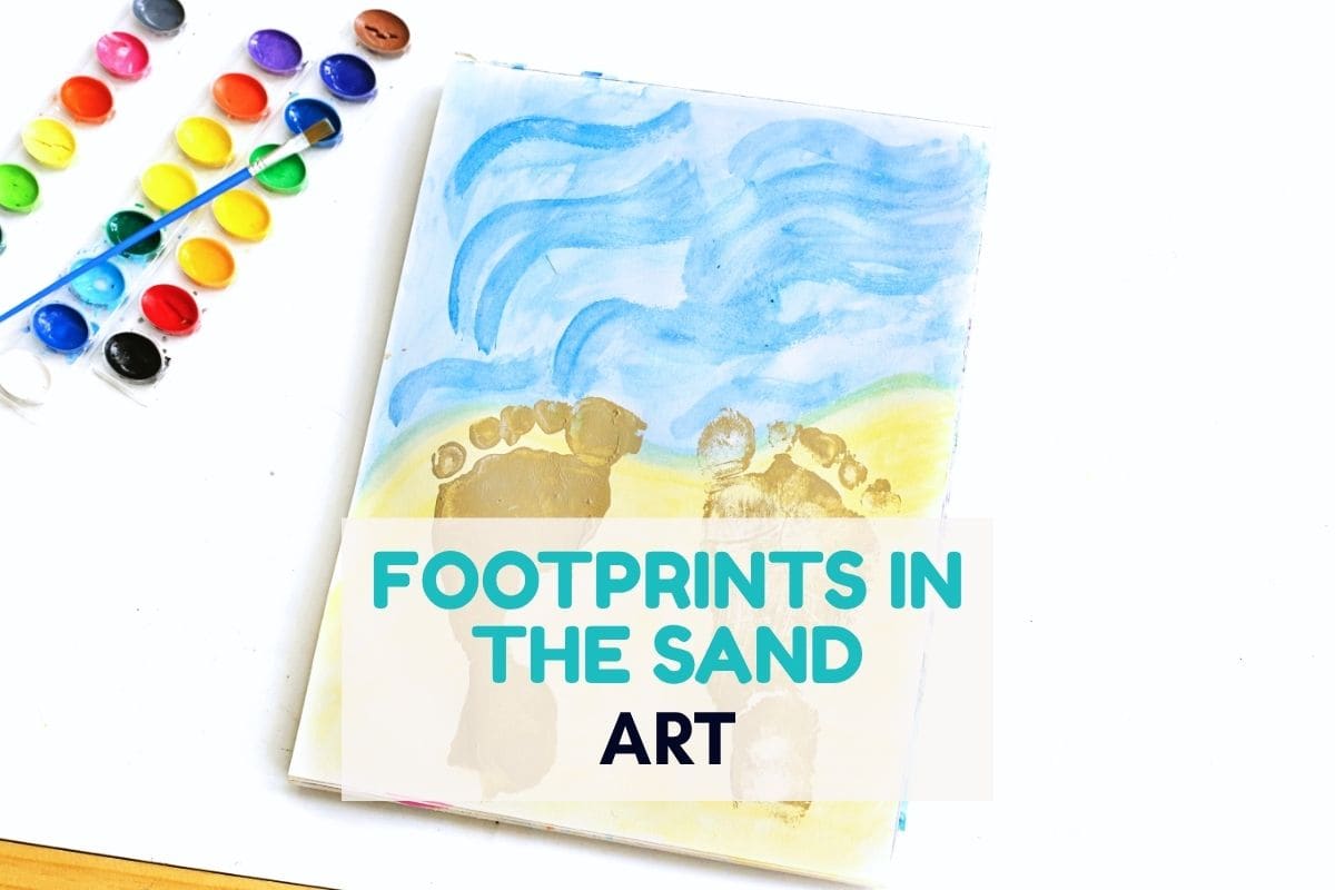 Child made beach themed artwork showing painted footprints stamped onto yellow sand beneath a blue sky with watercolor waves. A paint palette and brush sit beside the paper, and the image includes the text "FOOTPRINTS IN THE SAND ART".