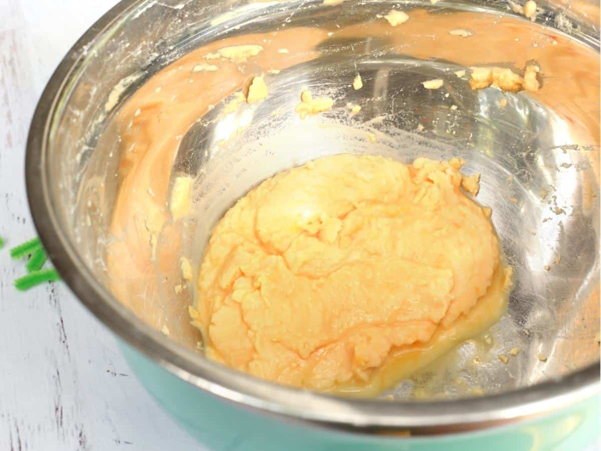 A bowl of thick orange dough mixture being prepared for the fizzy pumpkins experiment, with some mixture spread around the sides of the metal bowl.